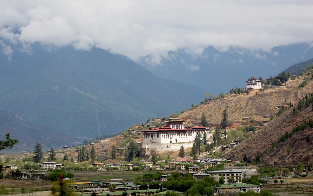 Scenic view of Paro Valley with Rinpung Dzong, surrounded by mountains and clouds in Bhutan.
