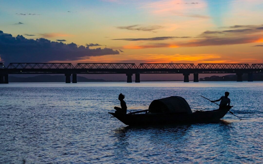 Silhouette of fishermen at sunset on the Brahmaputra with silhouetted boat and bridge in Assam, India.