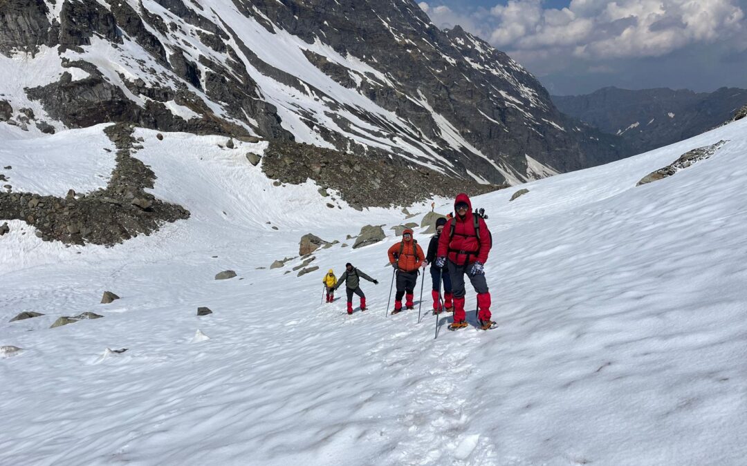 Adventurers trekking through snow in Hampta Pass, Himalayas. Experience majestic alpine scenery.