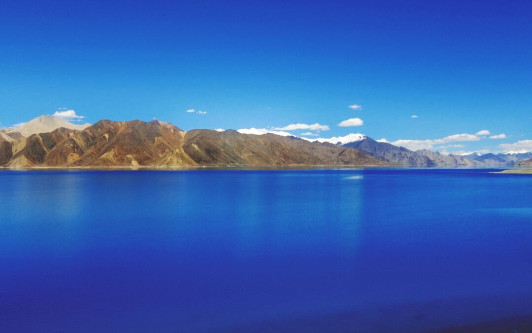 Idyllic view of Pangong Lake with mountains under a clear blue sky, showcasing nature's tranquility.