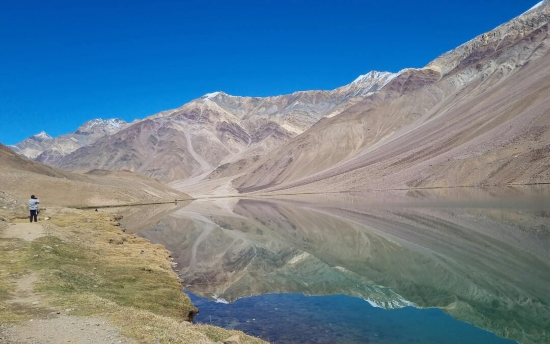 Stunning view of Chandratal Lake with majestic mountains and clear reflections, perfect for nature enthusiasts.