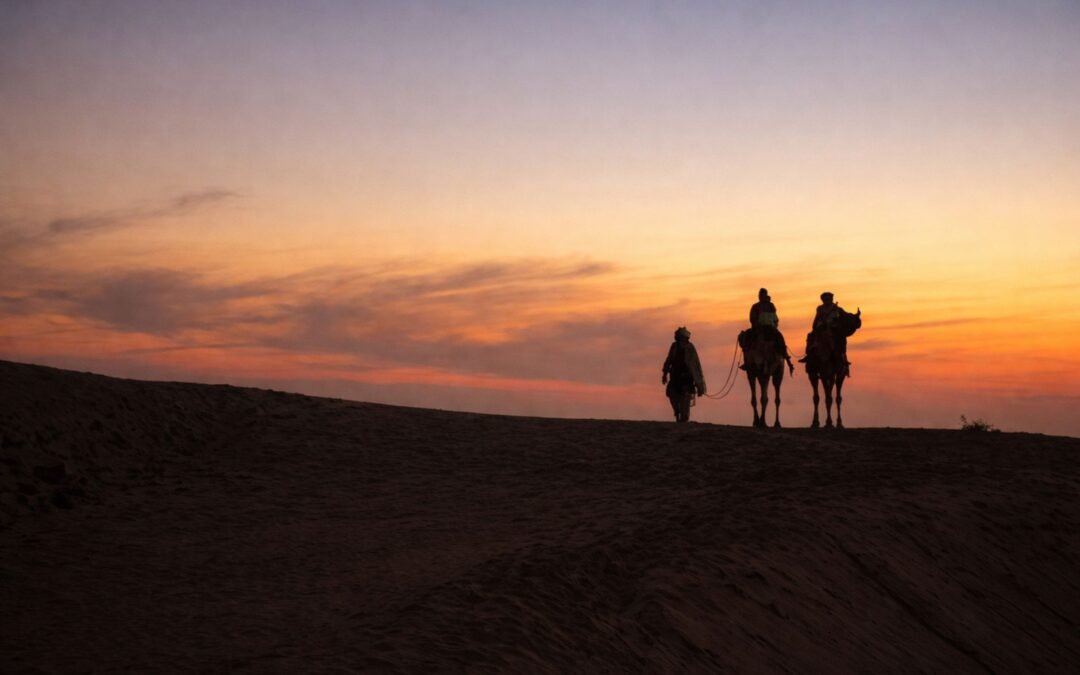 Silhouette of camels and riders during sunset in Sam, Rajasthan's Thar Desert.